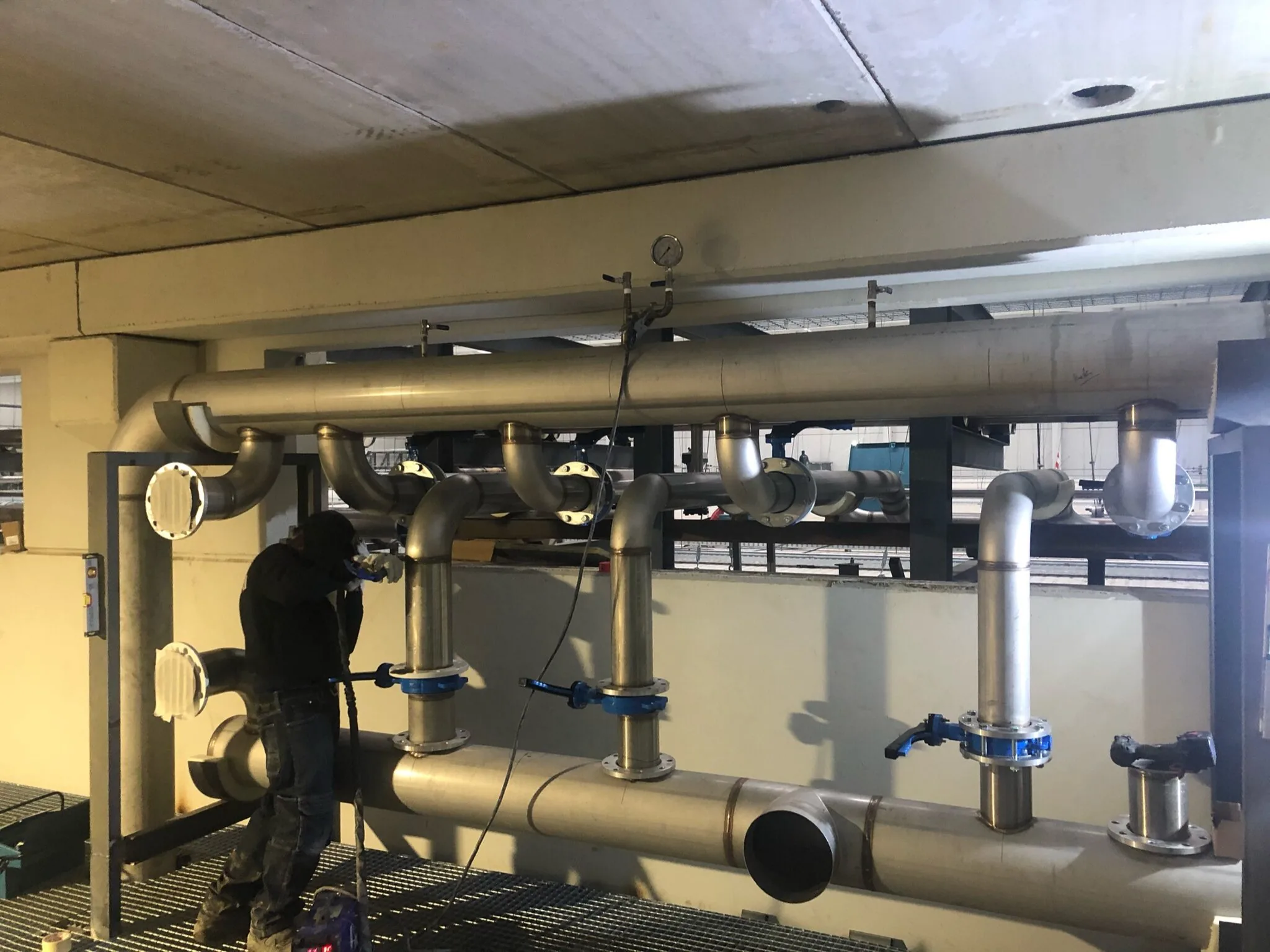 Operario trabajando en un colector de tubería de acero inoxidable con derivaciones en sala técnica