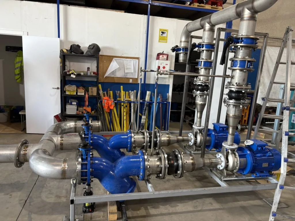 Skid prefabricado en taller con bombas azules, motores y tubería de acero inoxidable sobre bastidor galvanizado