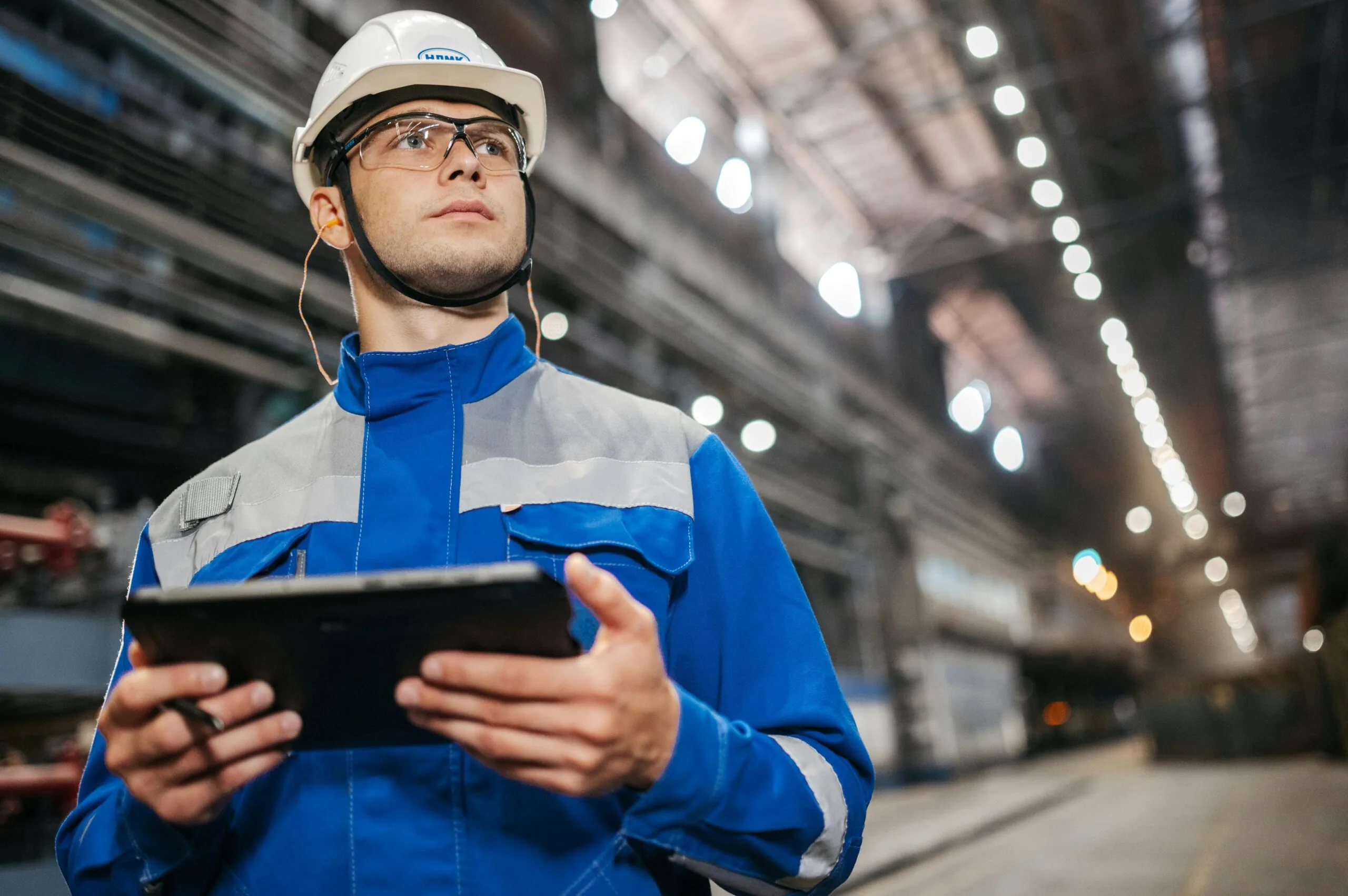 Técnico con casco y gafas de seguridad revisando datos en una tableta dentro de una nave industrial