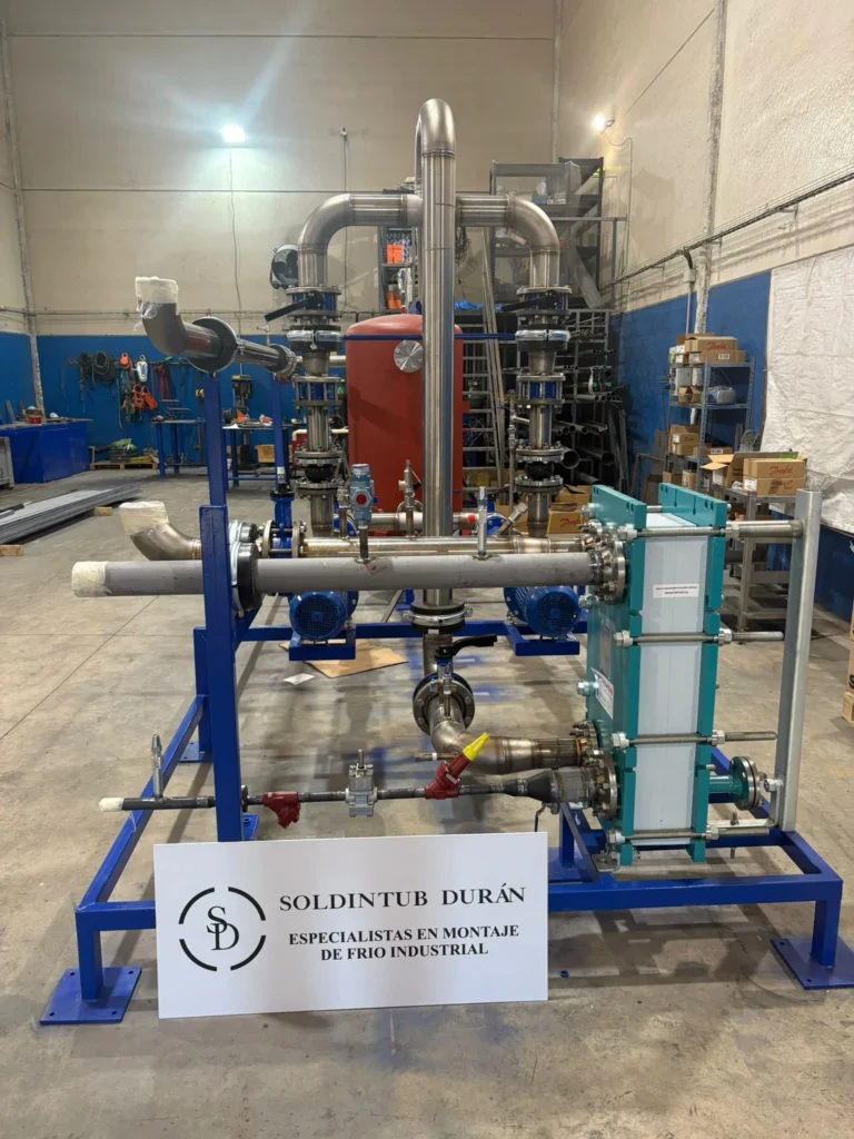 Skid de frío industrial con intercambiador de placas, bombas y colectores de acero inoxidable montado en taller