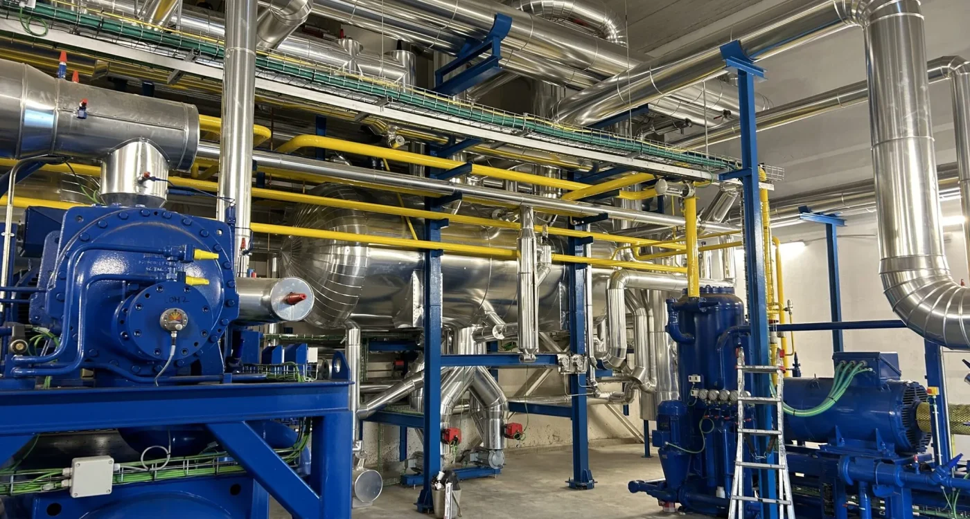 Sala de máquinas de frío industrial con compresores sobre bastidor azul y tubería aislada de gran diámetro