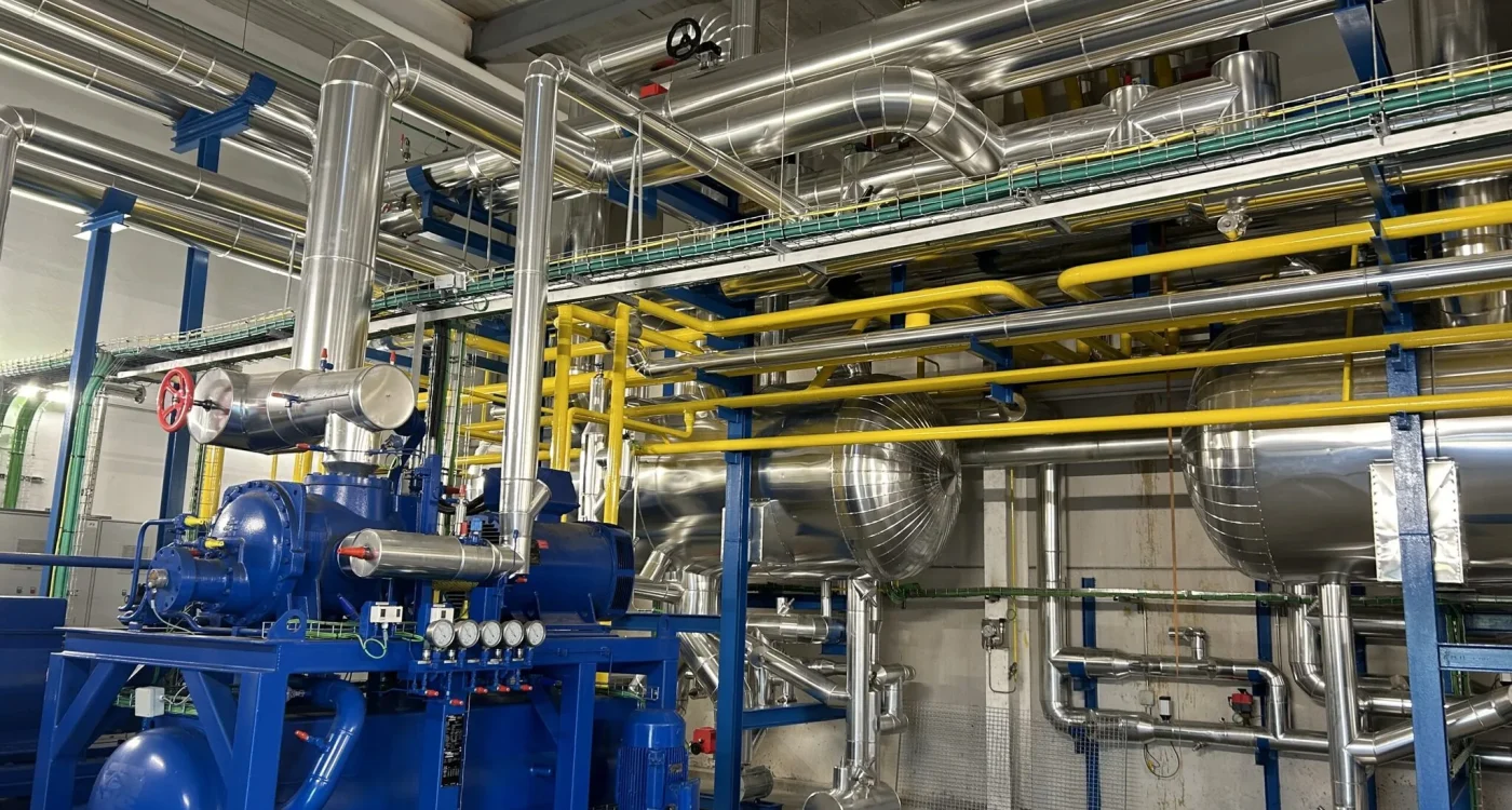 Sala de compresores de frío industrial con tubería aislada, colectores amarillos y separadores